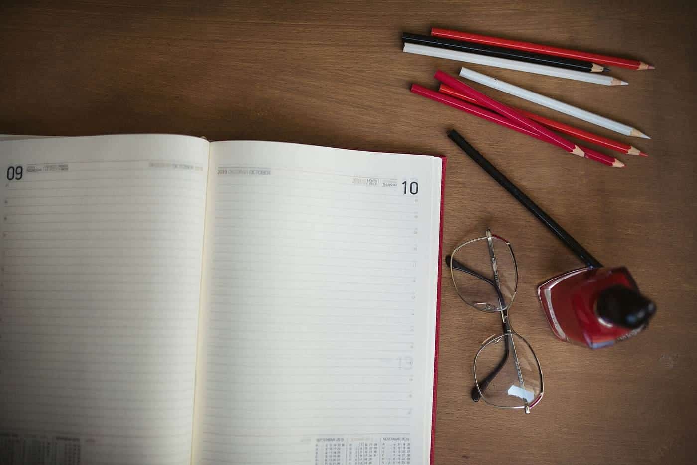 Open notebook, pencils and glasses on a wooden desk