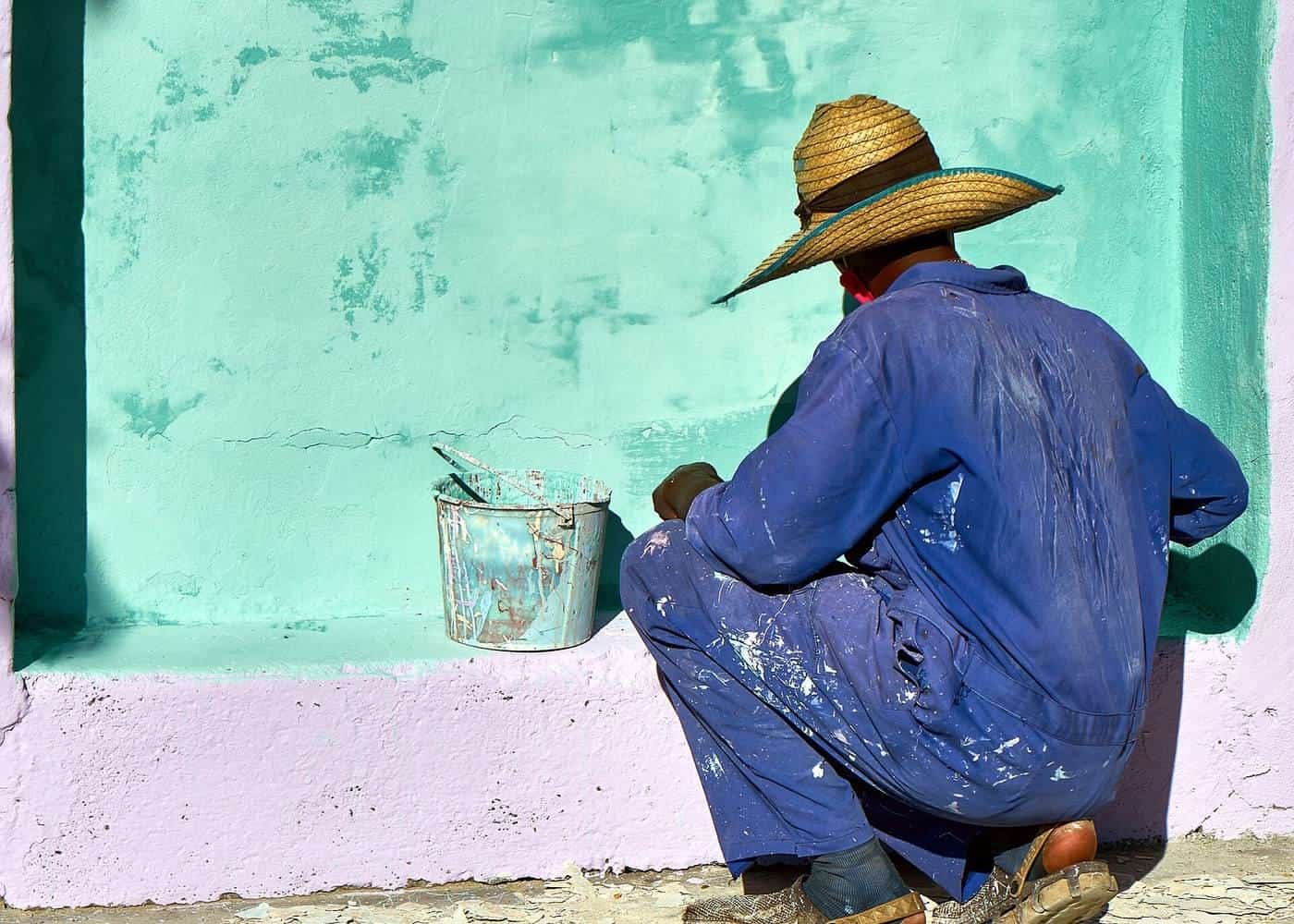 Painter in a straw hat and overalls painting a wall bright green