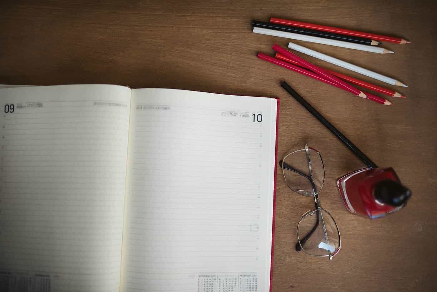 Open notebook, pencils and glasses on a wooden desk