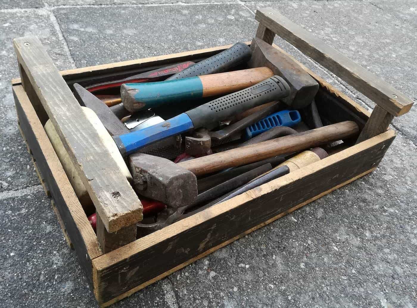 Wooden toolbox full of hammers and hand tools on a paved floor