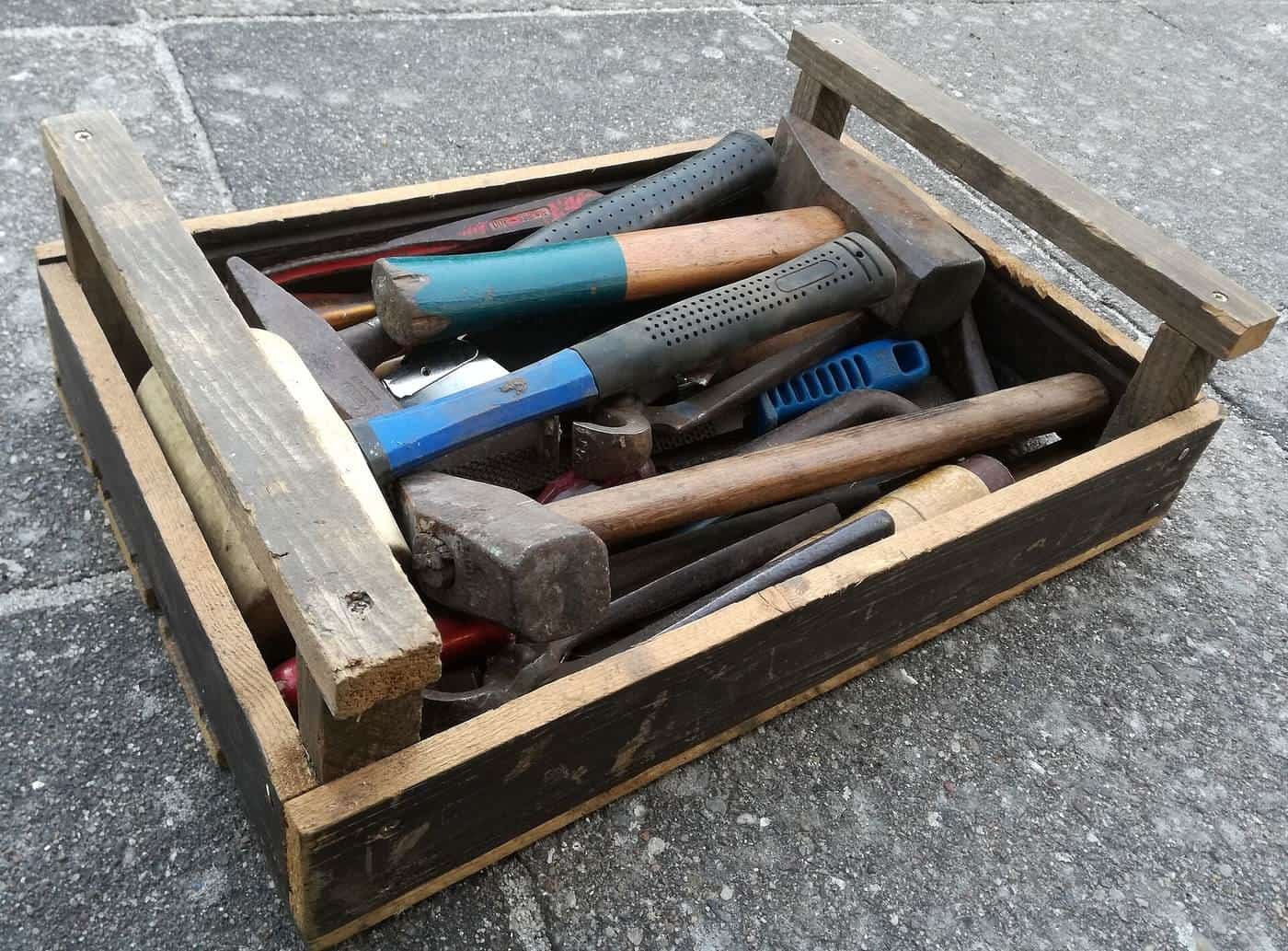 Wooden toolbox full of hammers and hand tools on a paved floor